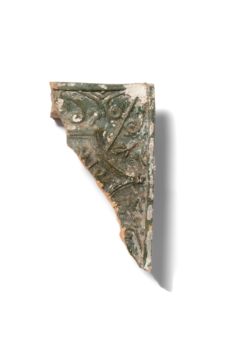 Fragment of a stove tile with stylised vegetal ornament and a throne backrest framing the central motif. The tile is made of hard, finely levigated clay, covered with green glaze, and decorated in relief. Second half of the 16th–17th century. 