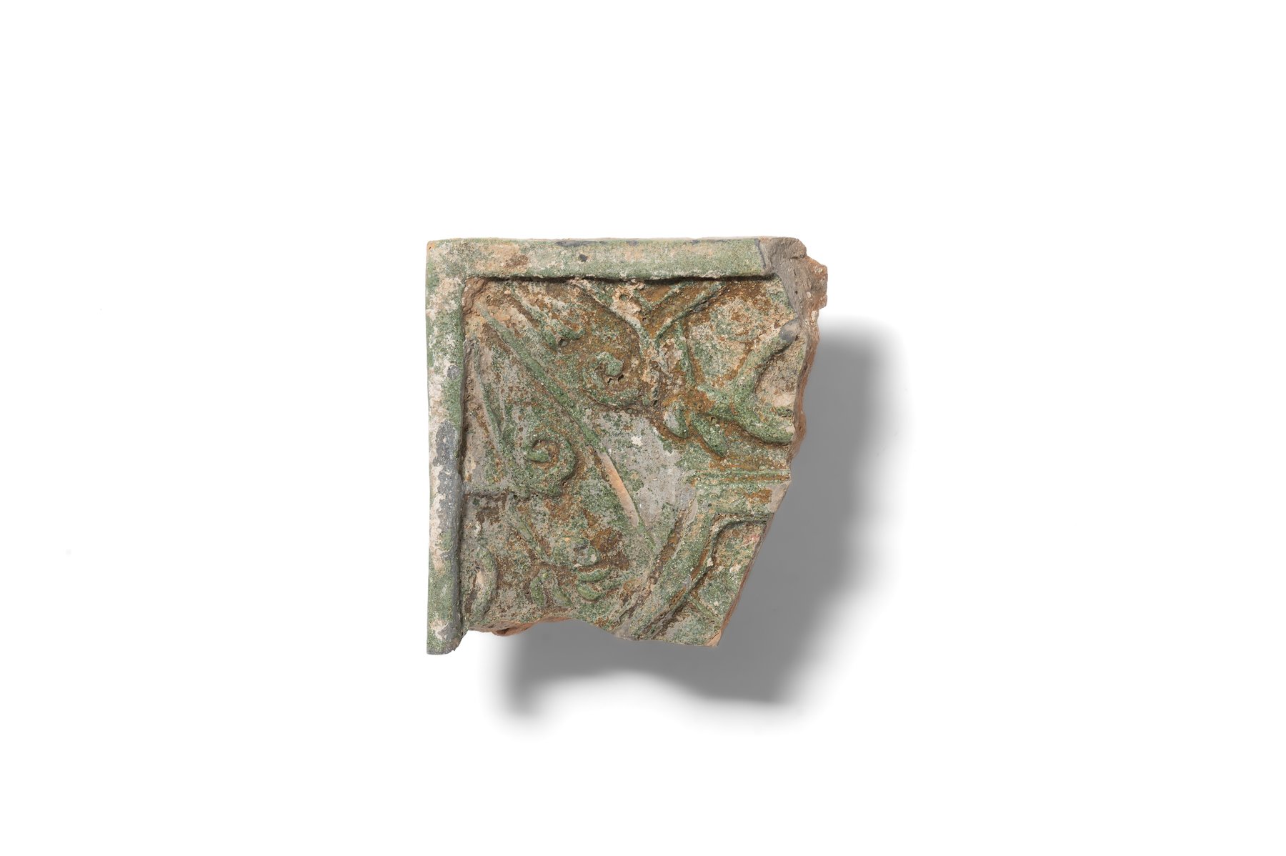 Fragment of a stove tile with stylised vegetal ornament; the central motif is framed by an irregular polygonal shape. The tile is made of hard, finely levigated clay and covered with green glaze. Second half of the 16th–17th century. 