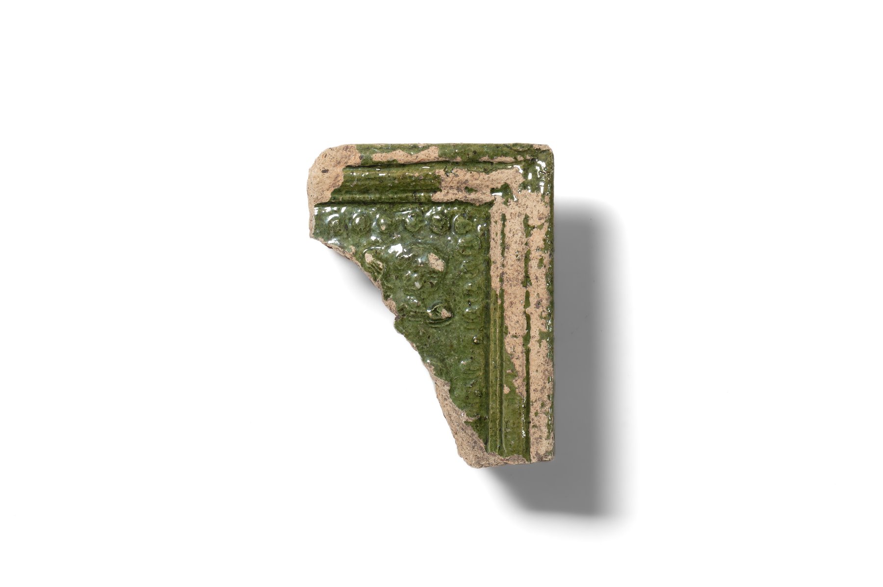 Fragment of a stove tile with a moulded frame and stylised vegetal ornament. A beaded border runs along the frame. The tile is made of hard, finely levigated clay and covered with green glaze. Second half of the 16th–17th century. 