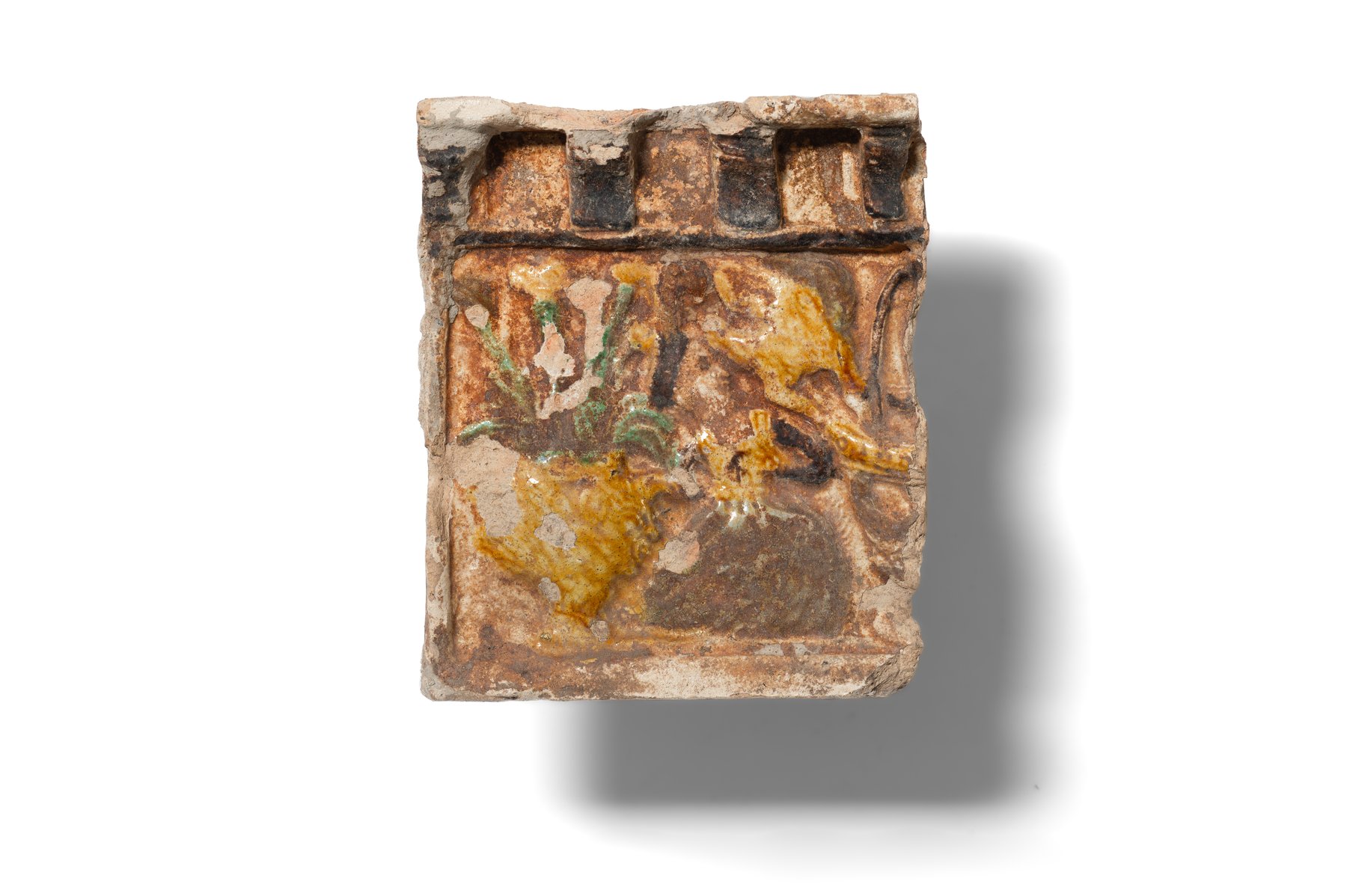 Fragment of a stove tile with a double frame. The upper outer frame is divided by projecting dark brown glazed vertical columns resembling supports for balconies or roofs. The tile depicts a vase of flowers and a woman wearing a headdress and a farthingale. It is made of hard, finely levigated clay and covered with green, yellow, and dark brown glazes. Second half of the 16th–17th century. 