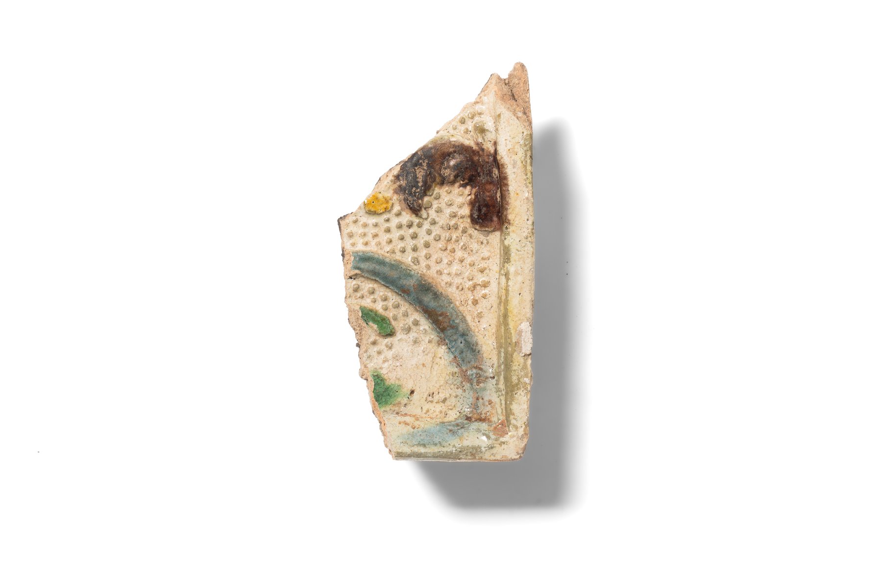 Fragment of a stove tile with a white bossed background and an unidentified motif executed in blue, brown, and green glazes. Second half of the 16th–17th century. 
